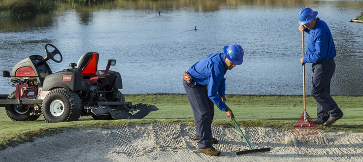 golf course maintenance crew raking bunker