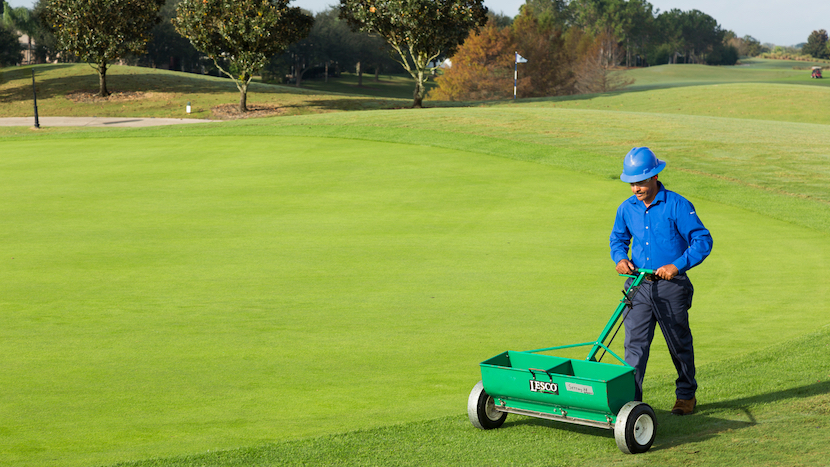 golf course maintenance crew member operating a spreader