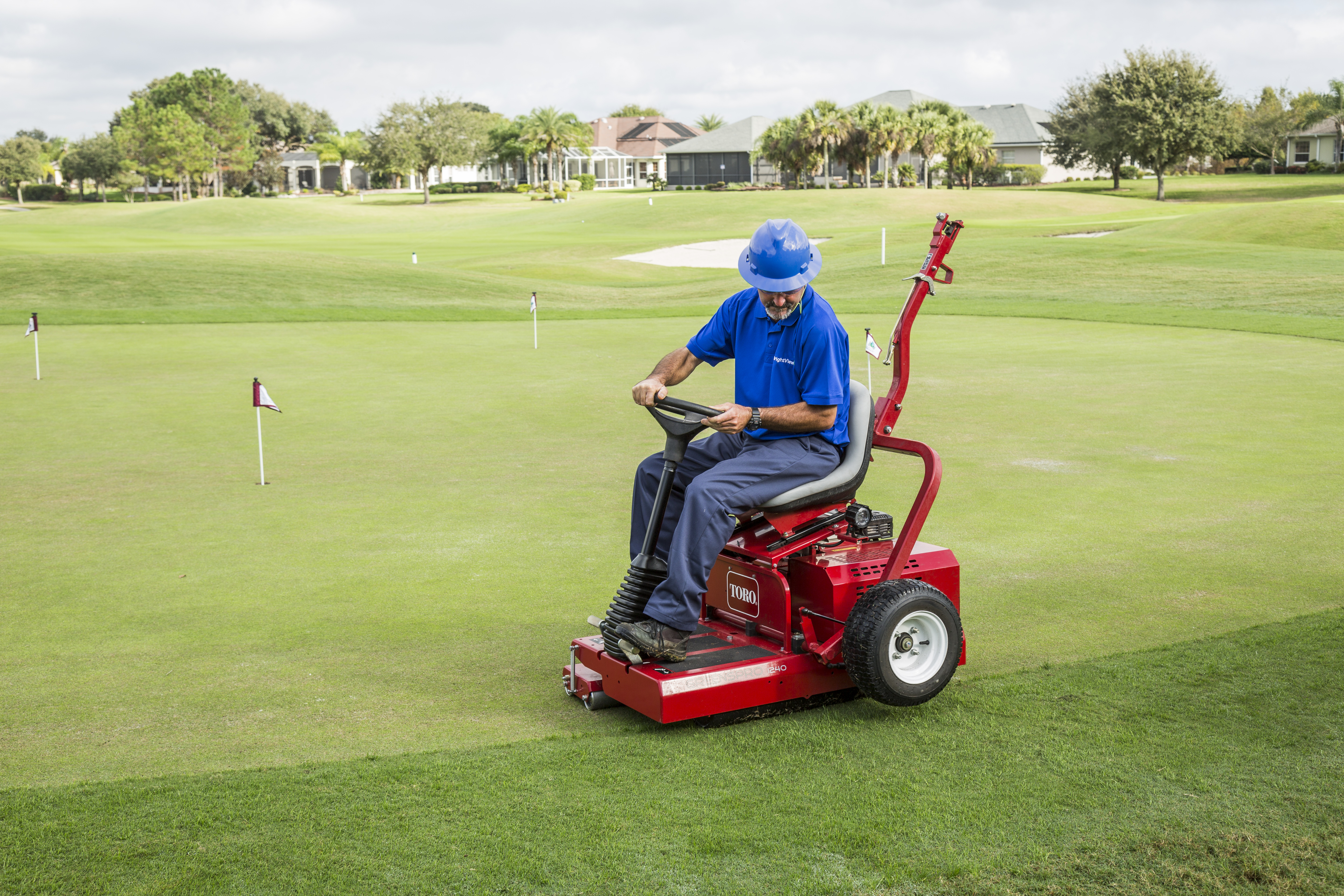 golf course maintenance crew member operating a greens roller