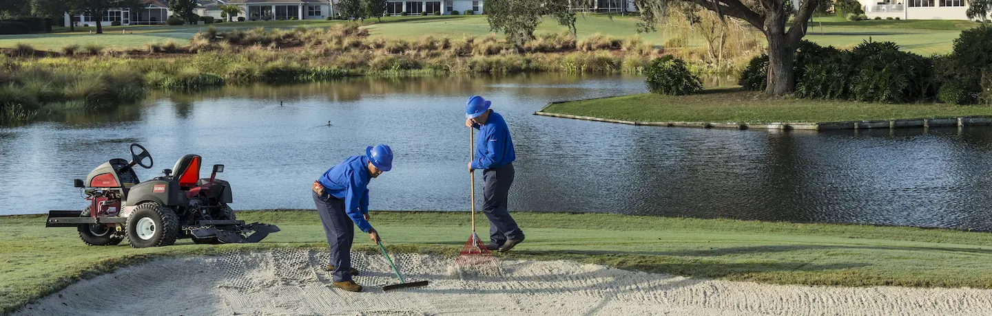 Two golf maintenance crew members raking a bunker