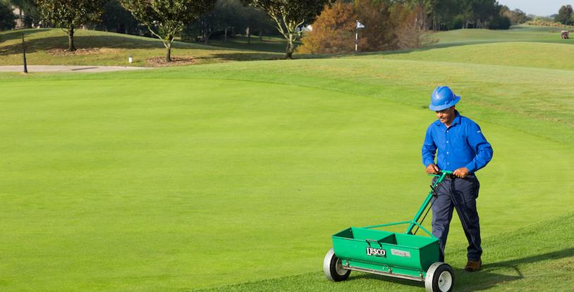 golf course maintenance crew member operating a spreader